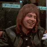 a man in a green leather jacket is smiling in front of a phone booth