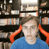 a boy in a blue shirt is sitting in a red chair in front of a bookshelf