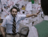 a man in a blue shirt and tie is smoking a cigarette in front of a wall covered in papers .