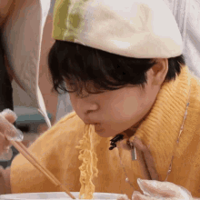 a person wearing a yellow sweater and a white beret is eating noodles with chopsticks