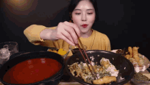 a woman in a yellow sweater is holding chopsticks over a bowl of food