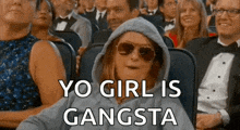 a woman wearing sunglasses and a hoodie is sitting in a crowd of people and says `` yo girl is gangsta '' .