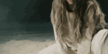 a woman with long hair is sitting on a beach