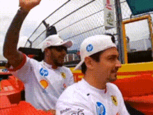 two men wearing white shirts and hats are sitting in a stadium .