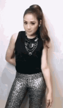 the woman is wearing a black tank top and silver pants .