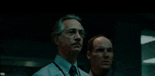 two men standing next to each other in a dark room looking at something .