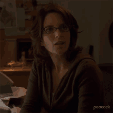 a woman wearing glasses is sitting in a dark room with peacock written on the bottom