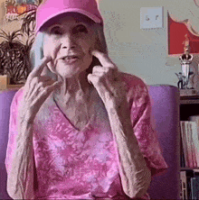 an elderly woman wearing a pink hat and a pink shirt is making a peace sign
