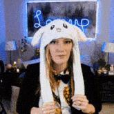 a woman wearing a bunny hat with moving ears is sitting in front of a neon sign .