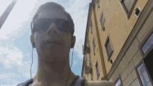 a man wearing sunglasses and ear buds is standing in front of a building