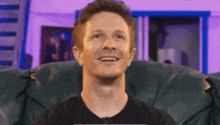 a man is smiling while sitting in a chair in front of a purple wall .