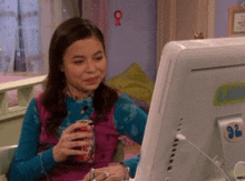 a girl is sitting in front of a computer and drinking a coke .