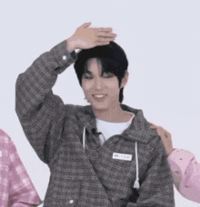 a young man in a plaid shirt is smiling and holding his hand to his head .