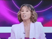 a woman in a white jacket is sitting in front of a purple backdrop