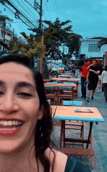 a woman is smiling in front of a row of tables on a sidewalk