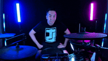 a man in a black shirt with the letter j on it stands in front of a drum set