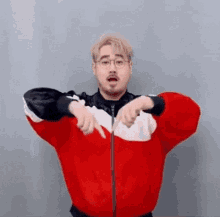 a man wearing a red and white jacket and glasses is pointing at the camera .