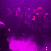 a dj playing music in front of a crowd with purple lights behind him