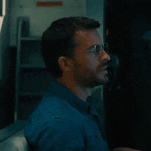 a man wearing glasses and a blue shirt looks at something