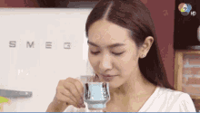 a woman drinking from a cup in front of a smeg fridge