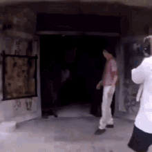 a man in a pink shirt is standing in a dark room while a cameraman takes a picture .