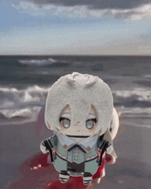 a stuffed animal with white hair and blue eyes standing on a beach