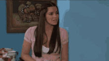 a woman in a pink shirt is sitting in front of a picture of a man and woman