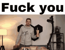 a man is standing in front of a microphone in a room holding a cup and giving the middle finger .