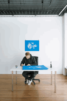 a man is sitting at a desk with a blue poster on the wall above him