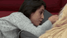 a woman in a grey sweater is laying on a red couch with a dog .