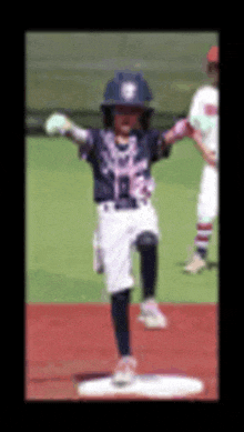 a young boy in a baseball uniform is standing on a base with his arms outstretched .