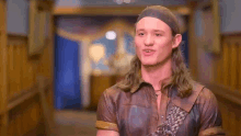a young man with long hair is wearing a leather shirt and a bandana .
