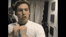 a man in a white shirt is adjusting his tie in front of a mirror in a room .