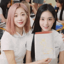 two girls are posing for a picture and one is holding a book with a picture of a duck on it