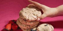 a woman 's hand reaches for a stack of cookies with strawberries and blueberries in the background
