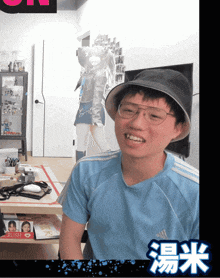 a man wearing glasses and a hat is smiling in front of a poster of a girl