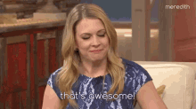 a woman in a blue dress is sitting on a couch and saying `` that 's awesome ! ''