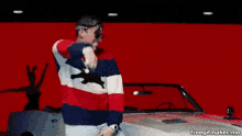 a man in a striped sweater is standing in front of a red car .