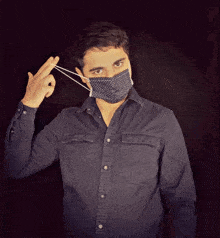 a man wearing a black shirt and a black face mask is pointing at himself