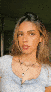 a woman wearing a grey shirt and a necklace with a round pendant