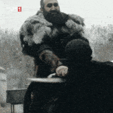 a man in a fur coat holds a knife in front of a woman with trt 1 written on the bottom