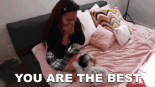 a woman is sitting on a bed with a dog and the words `` you are the best '' are written above her .