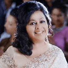 a woman in a saree is smiling at the camera while sitting in a crowd .