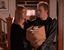 a man and a woman standing next to each other holding a bag of food