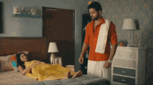 a man in a red shirt is standing next to a woman in a yellow dress on a bed