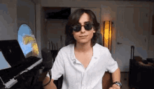 a young man wearing sunglasses is standing in front of a piano .