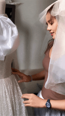 a woman wearing a veil is looking at a wedding dress on a mannequin