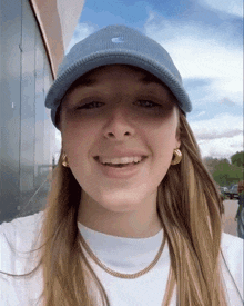 a woman wearing a blue nike hat and a gold necklace smiles