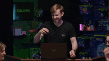 a man wearing a black shirt with rh on it stands in front of a laptop