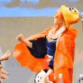 a woman wearing an orange cape and a yellow hat with a pumpkin face on it